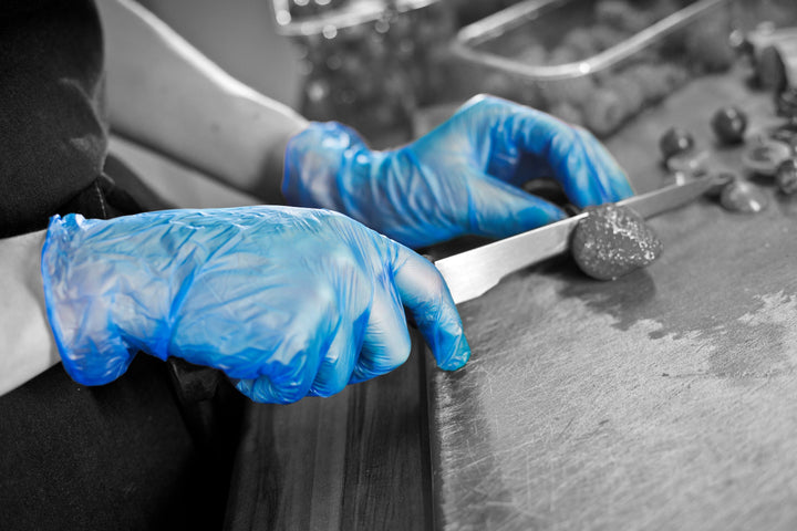 A Person Wearing a Pair of Blue GD13 Vinyl Gloves Using a Long Knife to Cut a Strawberry