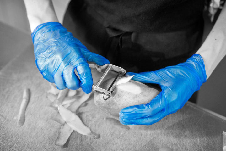 A Person Wearing a Pair of Blue GD13 Vinyl Gloves Using a Peeler to Peel a Potato